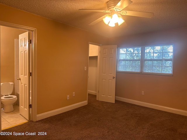 unfurnished bedroom featuring a textured ceiling, a walk in closet, carpet, ensuite bath, and ceiling fan