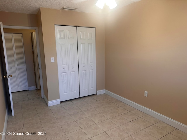 unfurnished bedroom with light tile patterned floors, ceiling fan, a closet, and a textured ceiling