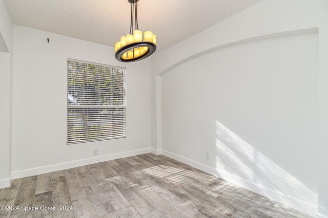 unfurnished room featuring a textured ceiling, light hardwood / wood-style flooring, and a chandelier