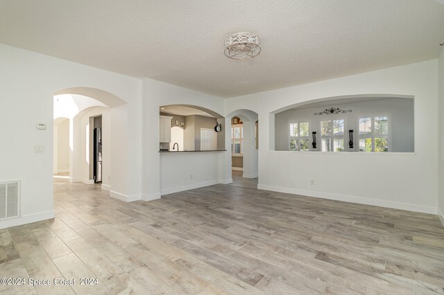 unfurnished living room featuring light hardwood / wood-style flooring and a textured ceiling