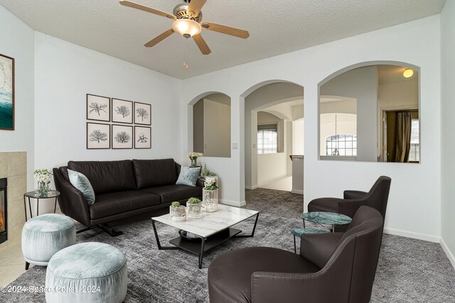 living room with a textured ceiling, carpet, a tiled fireplace, and ceiling fan