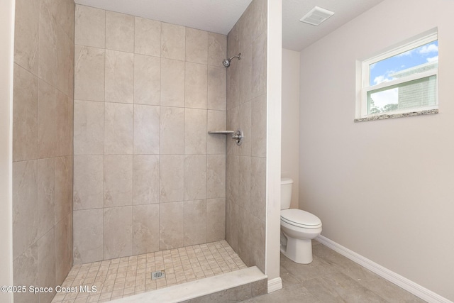 bathroom with toilet, tile patterned flooring, and tiled shower