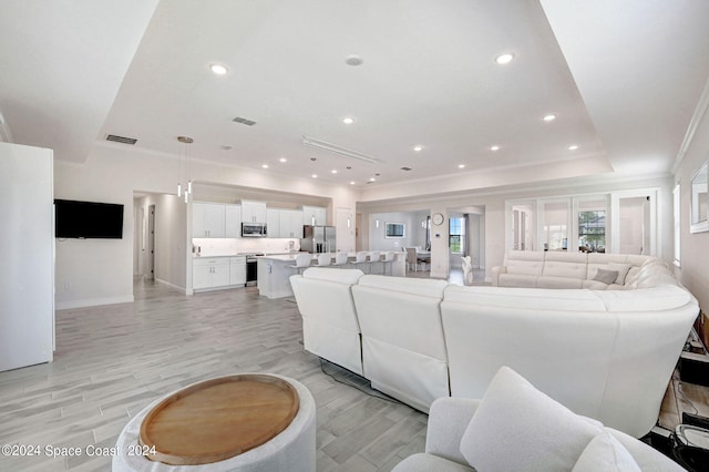 living room with crown molding, light hardwood / wood-style flooring, and a raised ceiling