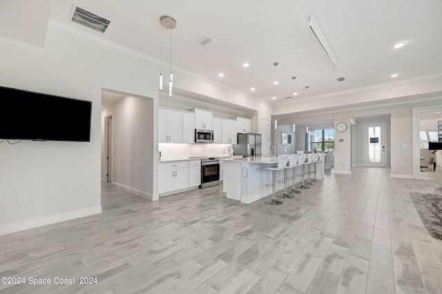 kitchen with appliances with stainless steel finishes, white cabinetry, an island with sink, a breakfast bar, and decorative light fixtures