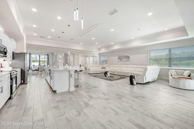 kitchen featuring decorative light fixtures, white cabinetry, appliances with stainless steel finishes, a tray ceiling, and a breakfast bar area