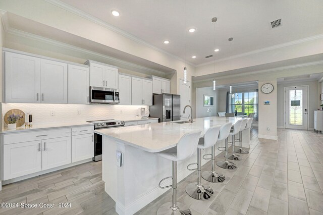 kitchen featuring an island with sink, white cabinets, appliances with stainless steel finishes, and decorative light fixtures