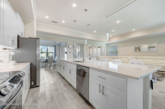 kitchen featuring white cabinets, an island with sink, appliances with stainless steel finishes, and decorative light fixtures