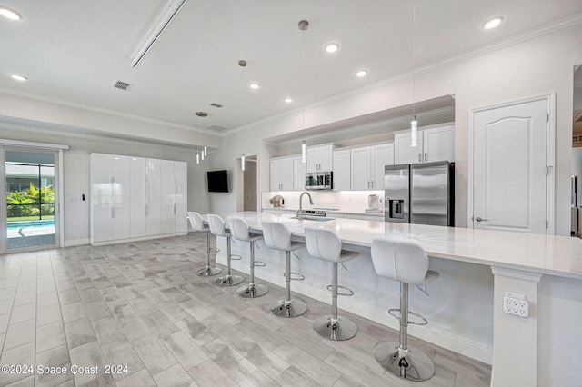 kitchen with white cabinets, decorative light fixtures, appliances with stainless steel finishes, a spacious island, and a kitchen bar