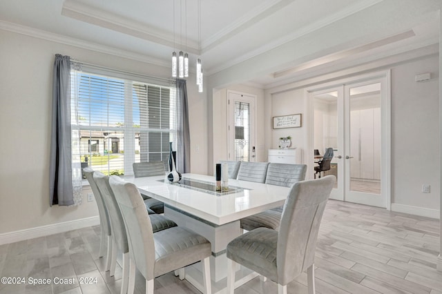 dining space featuring ornamental molding, light wood-type flooring, a tray ceiling, and french doors