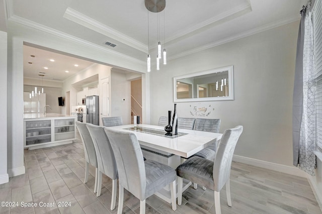 dining space featuring light wood-type flooring, ornamental molding, a tray ceiling, and sink