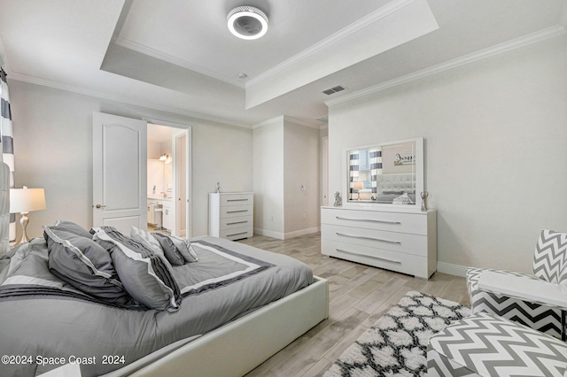 bedroom with ornamental molding, light wood-type flooring, ensuite bath, and a raised ceiling