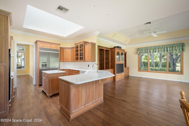 kitchen with dark wood-type flooring, kitchen peninsula, built in fridge, ceiling fan, and ornamental molding