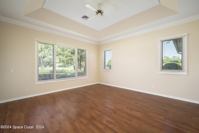 unfurnished room featuring a tray ceiling, dark hardwood / wood-style floors, ceiling fan, and plenty of natural light