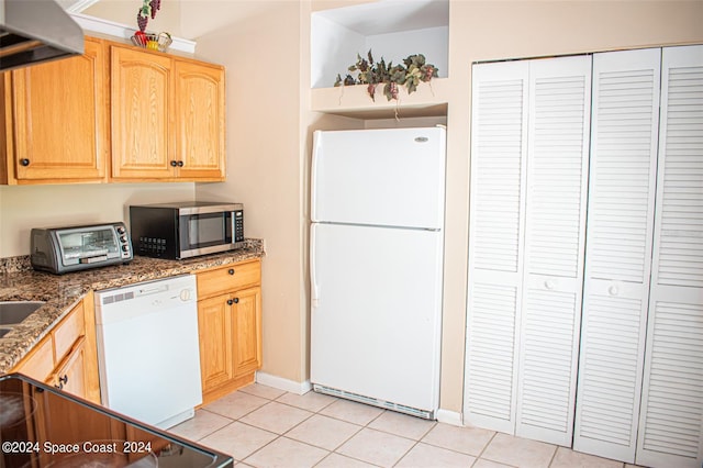 kitchen with white appliances, light brown cabinetry, light tile patterned floors, ventilation hood, and dark stone counters