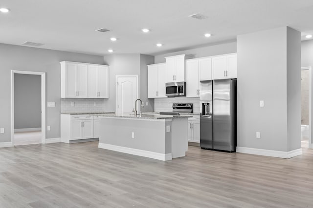 kitchen featuring appliances with stainless steel finishes, a center island with sink, white cabinets, and light hardwood / wood-style floors