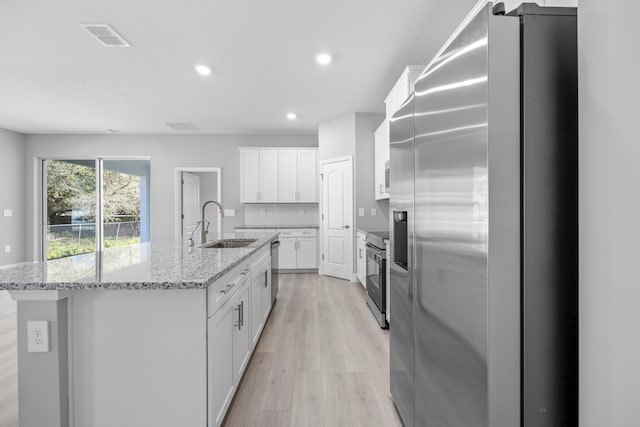 kitchen with an island with sink, stainless steel appliances, sink, and white cabinetry