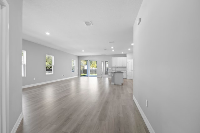 unfurnished living room with a textured ceiling, sink, and light hardwood / wood-style floors