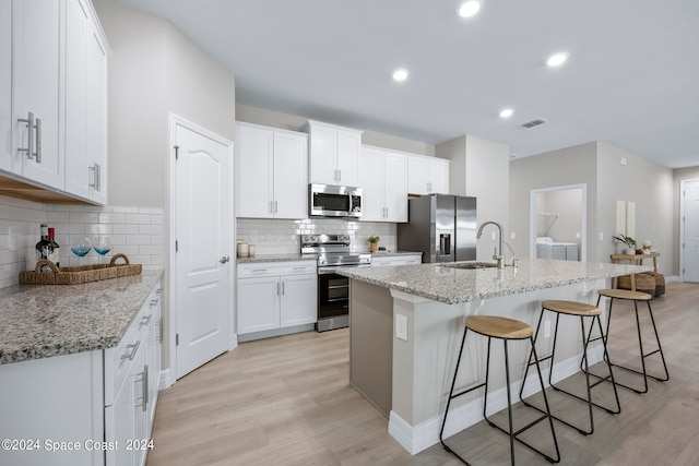 kitchen featuring white cabinetry, washing machine and dryer, light stone counters, appliances with stainless steel finishes, and light hardwood / wood-style floors