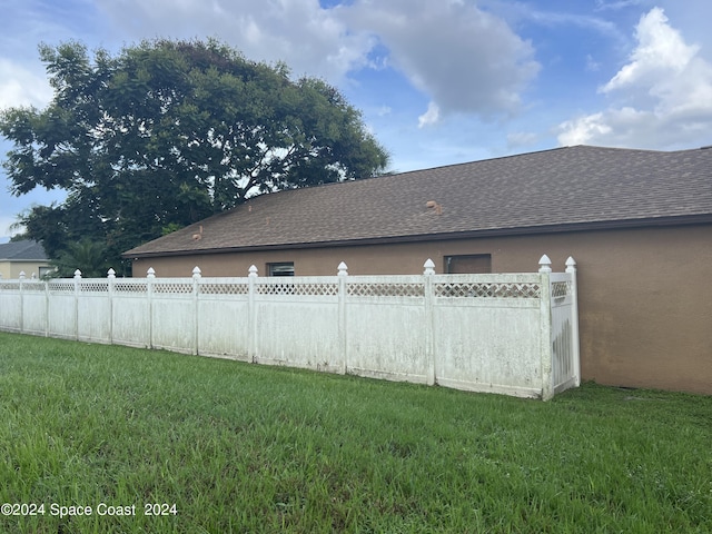 view of home's exterior with stucco siding, a lawn, a shingled roof, and fence