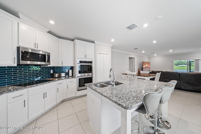 kitchen with a kitchen island with sink, dark stone countertops, white cabinetry, sink, and appliances with stainless steel finishes