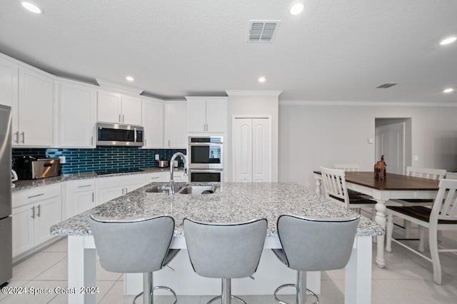 kitchen featuring appliances with stainless steel finishes, a center island with sink, white cabinetry, and light tile patterned flooring