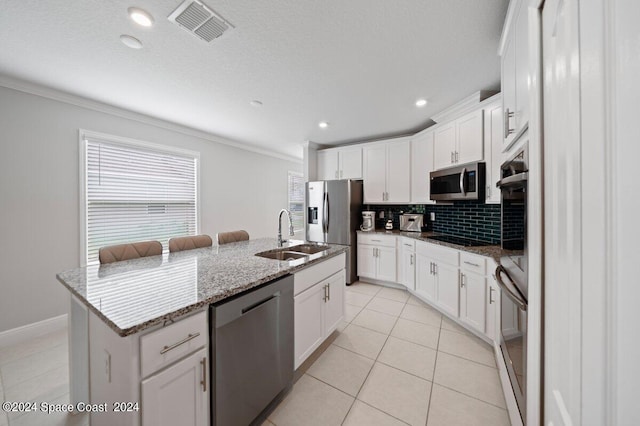 kitchen with white cabinets, appliances with stainless steel finishes, light stone countertops, sink, and a center island with sink