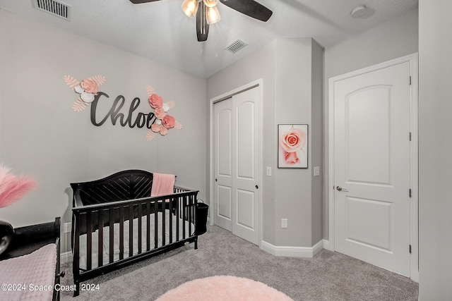 carpeted bedroom with ceiling fan, a nursery area, a textured ceiling, and a closet