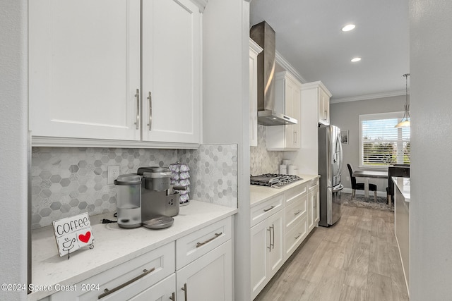 kitchen featuring crown molding, wall chimney range hood, stainless steel appliances, and white cabinets