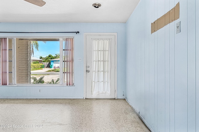 entryway with wood walls, ceiling fan, and a textured ceiling