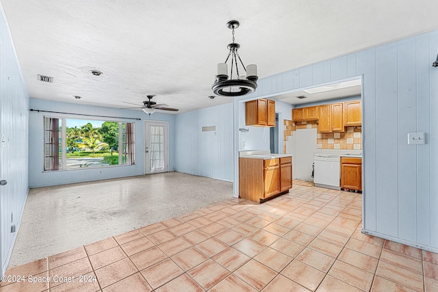 kitchen featuring white dishwasher, hanging light fixtures, wooden walls, backsplash, and ceiling fan with notable chandelier