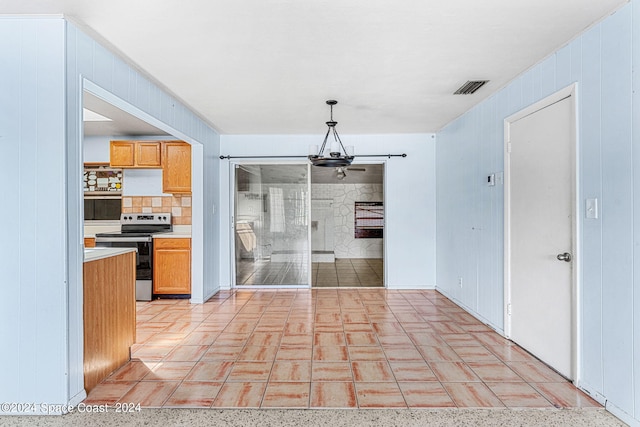 kitchen featuring decorative backsplash, stainless steel electric stove, light tile patterned floors, pendant lighting, and wooden walls