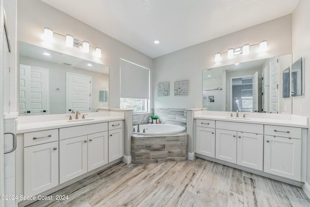 bathroom with a relaxing tiled tub, wood-type flooring, and vanity