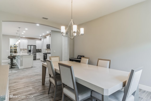 dining space with a notable chandelier, sink, and light hardwood / wood-style flooring