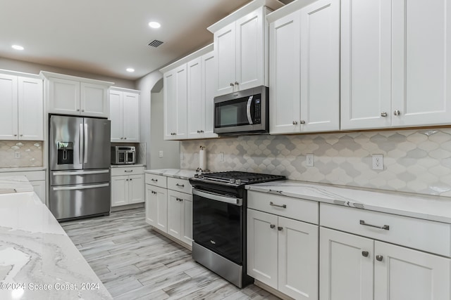 kitchen featuring decorative backsplash, appliances with stainless steel finishes, light stone countertops, light hardwood / wood-style flooring, and white cabinetry