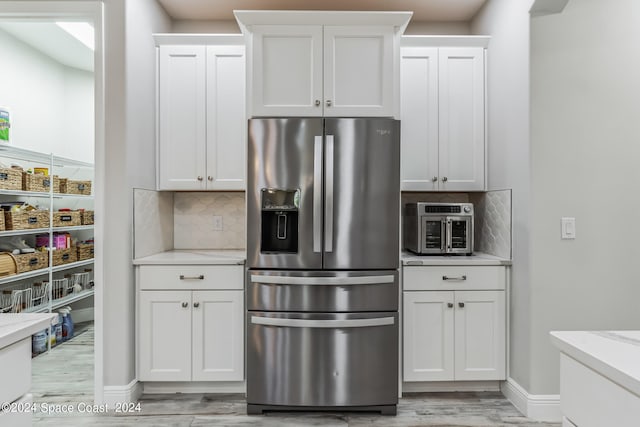 kitchen featuring stainless steel fridge, backsplash, white cabinetry, and light stone counters