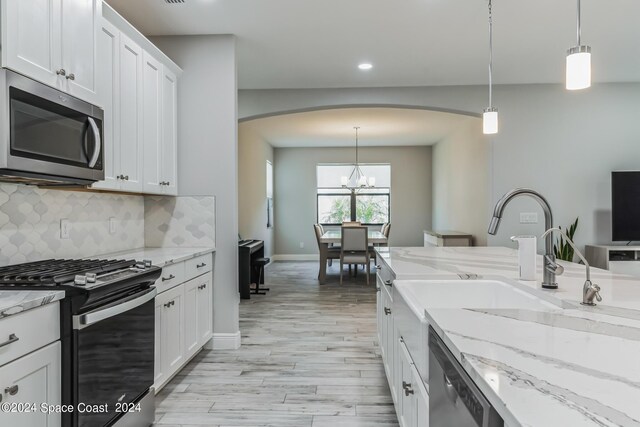 kitchen with white cabinets, light hardwood / wood-style floors, hanging light fixtures, and appliances with stainless steel finishes