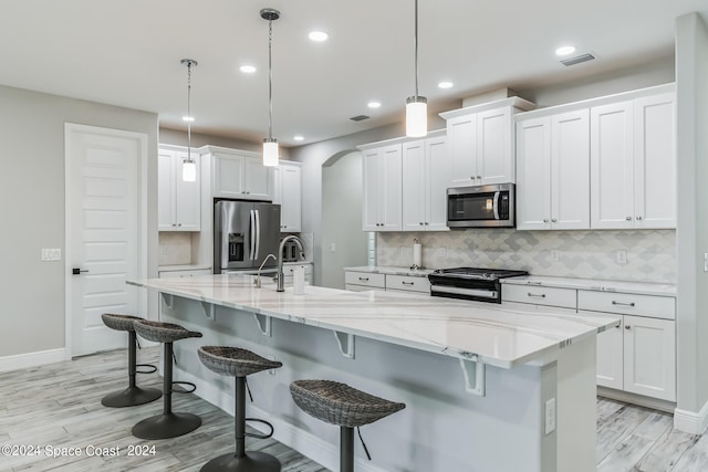 kitchen featuring pendant lighting, white cabinetry, a kitchen island with sink, and appliances with stainless steel finishes