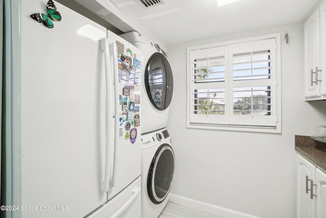 clothes washing area featuring cabinets and stacked washer / dryer