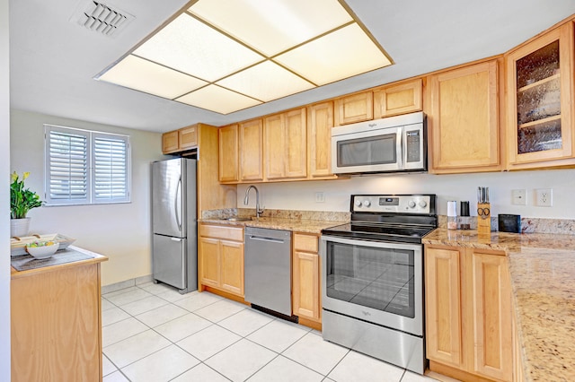 kitchen with light stone countertops, appliances with stainless steel finishes, light tile patterned floors, and light brown cabinetry