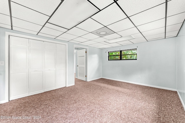 unfurnished bedroom with a paneled ceiling, carpet, and a closet