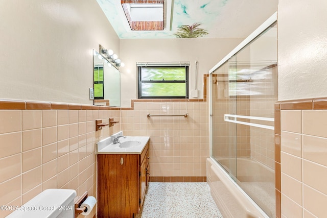 full bathroom with vanity, bath / shower combo with glass door, tile walls, toilet, and a skylight