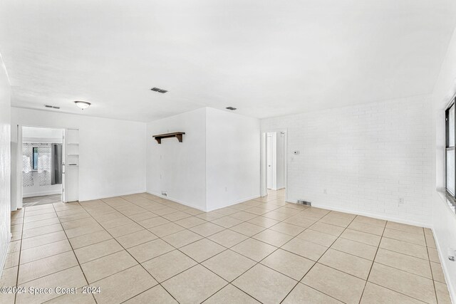 unfurnished room with brick wall and light tile patterned flooring