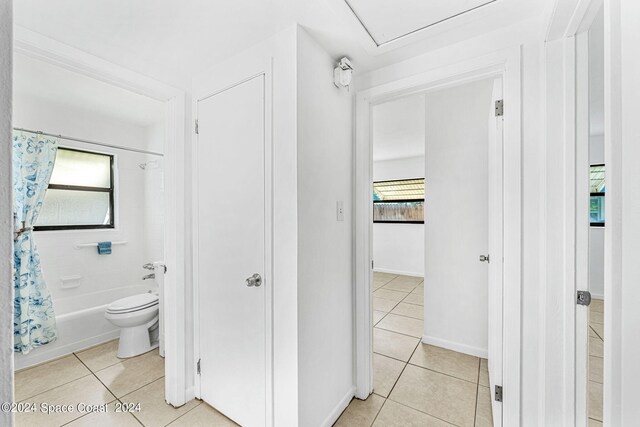 bathroom with tile patterned flooring, toilet, a wealth of natural light, and shower / bathtub combination with curtain