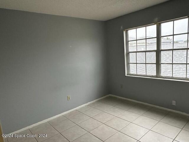 spare room featuring baseboards, a textured ceiling, and light tile patterned floors
