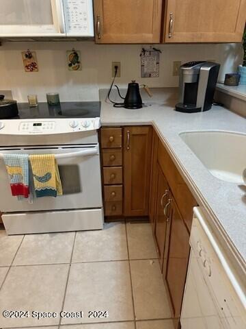 kitchen with light tile patterned flooring, light countertops, white appliances, a sink, and brown cabinetry
