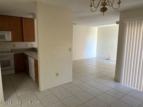 kitchen with light tile patterned floors, decorative light fixtures, a chandelier, and white appliances