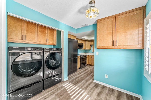 laundry area featuring cabinets, washing machine and dryer, a textured ceiling, and light hardwood / wood-style flooring