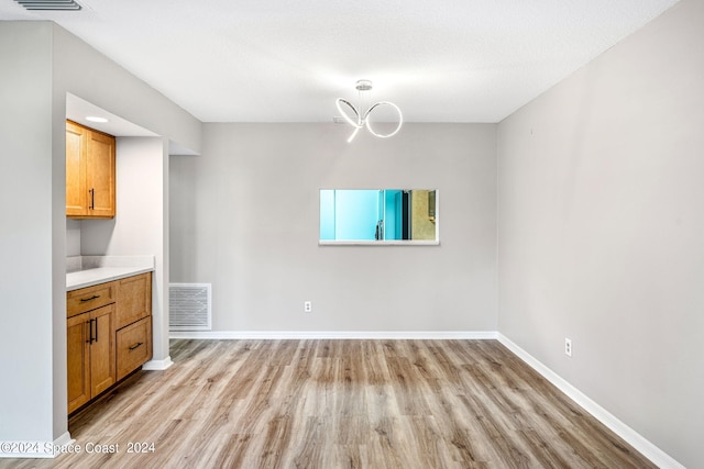 unfurnished dining area featuring light hardwood / wood-style floors, a textured ceiling, and an inviting chandelier