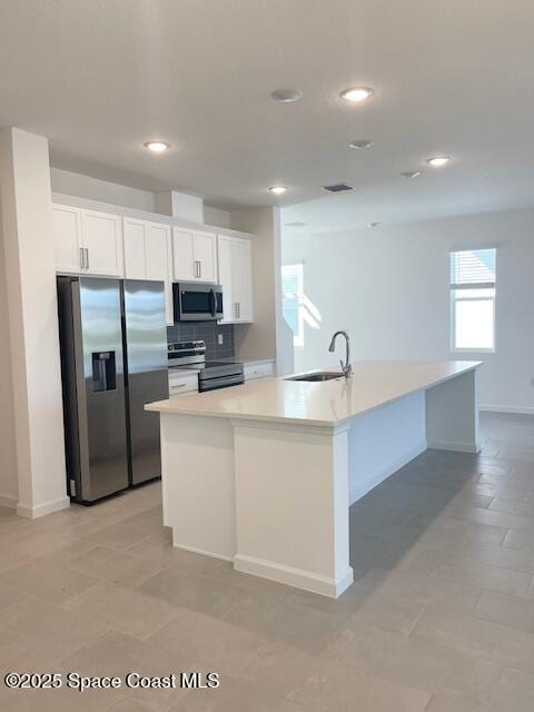 kitchen with backsplash, a center island with sink, appliances with stainless steel finishes, white cabinets, and a sink