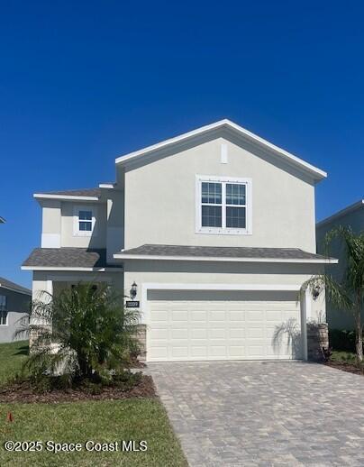 traditional-style home featuring stucco siding, decorative driveway, and a garage